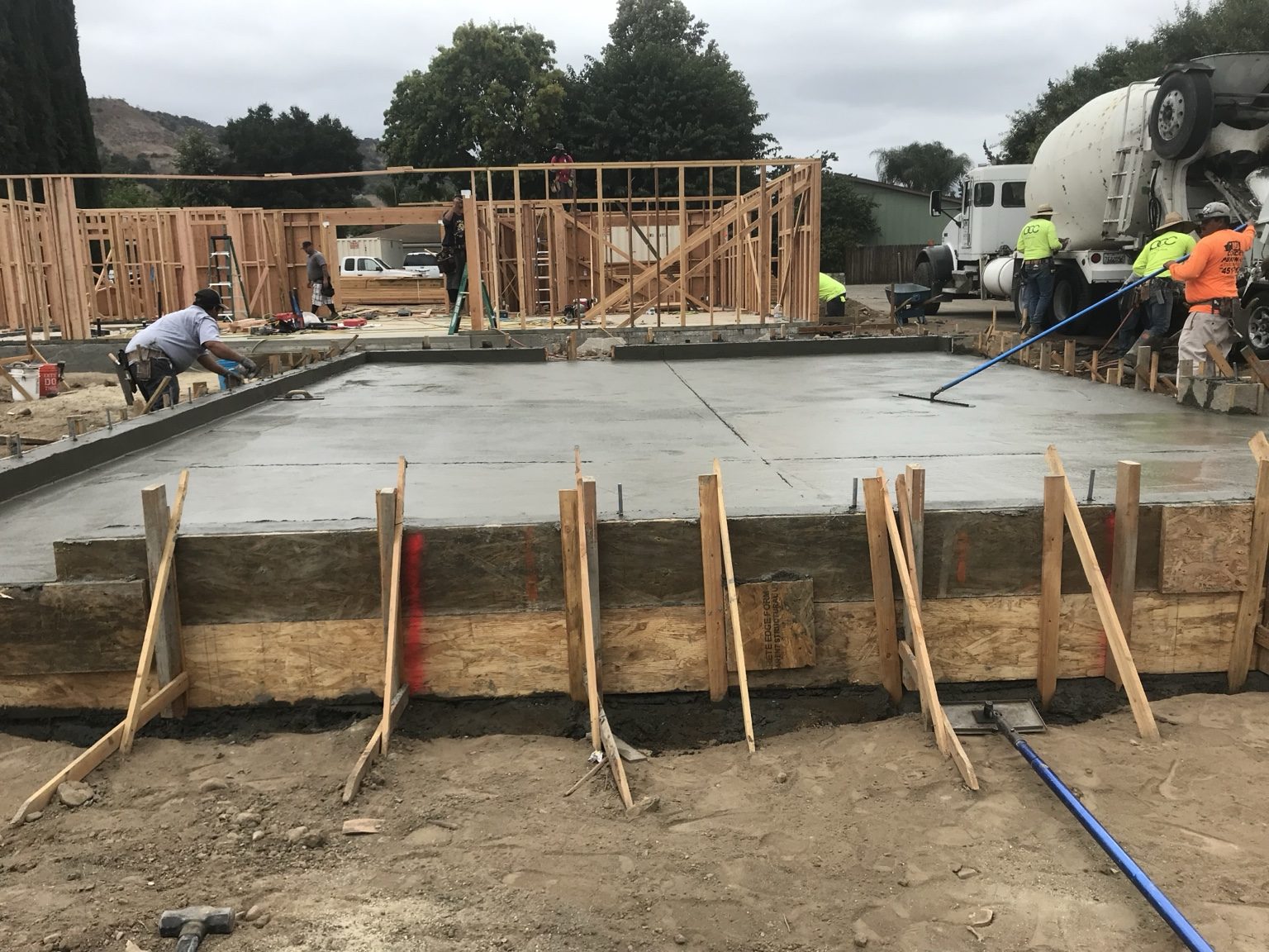 Crew finishing a freshly poured garage slab with house framing behind
