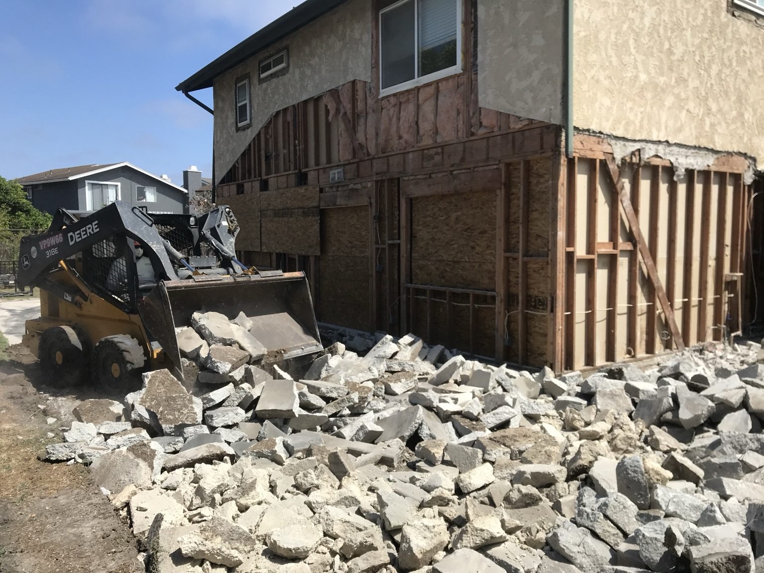 Skid steer clearing demolition debris beside the opened exterior walls of the house
