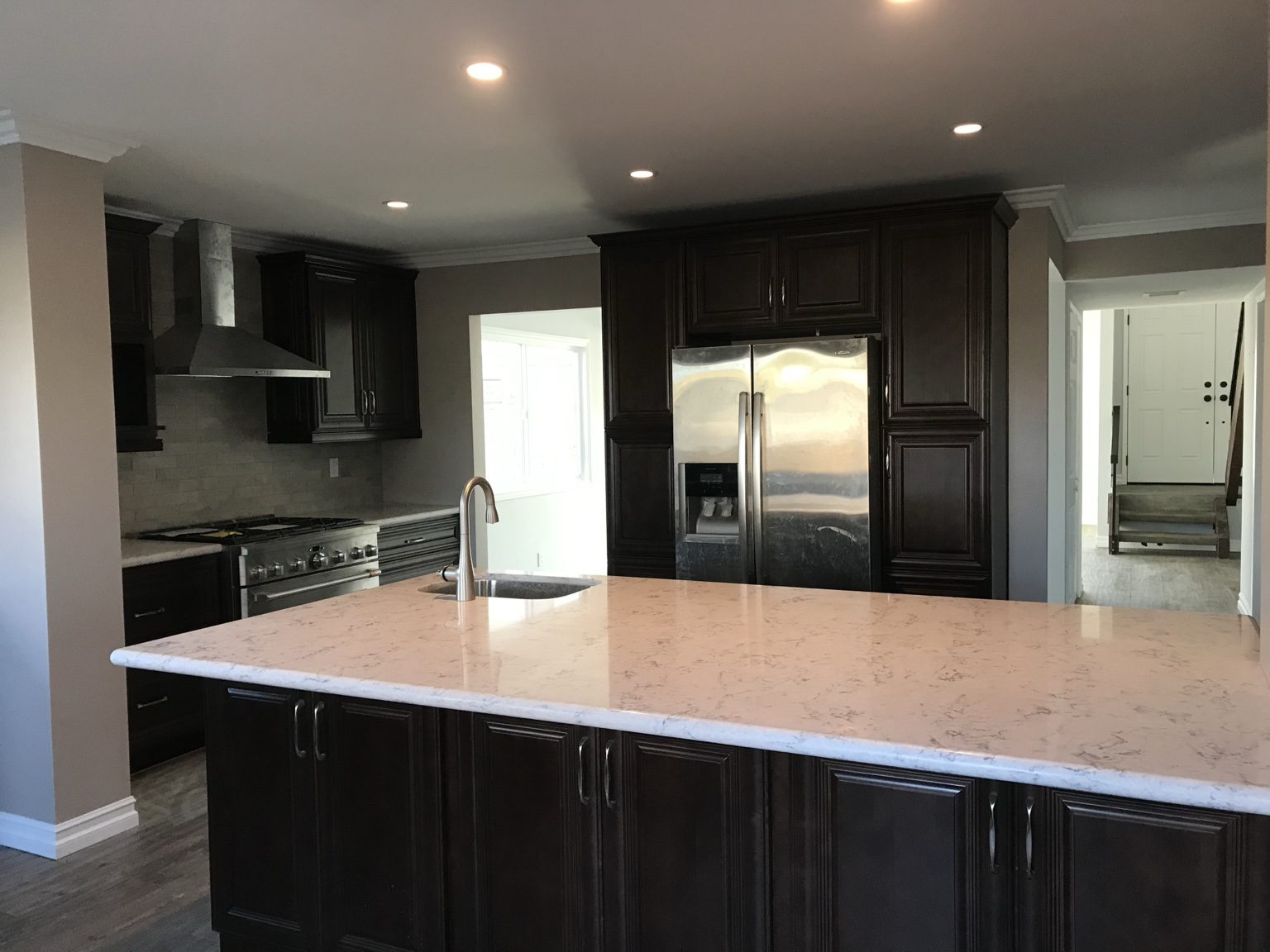 Expanded kitchen with dark maple cabinets, a large quartz island and stainless appliances